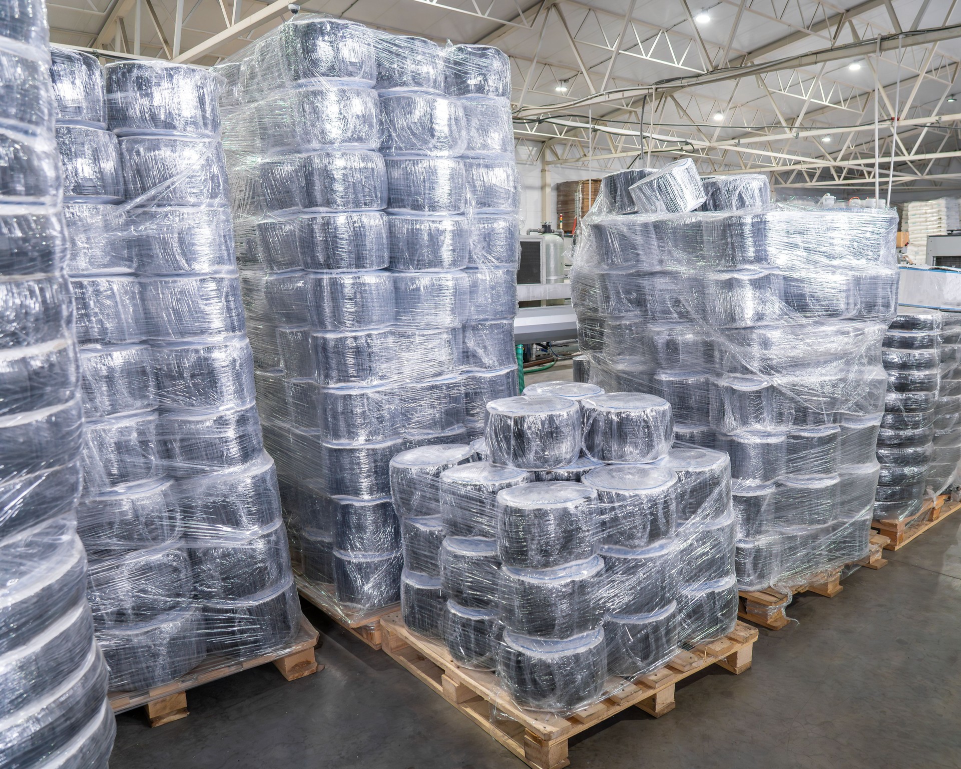 Stacks of plastic spools packed in stretch film on wooden pallets in modern warehouse. Industrial packaging, logistics and plastic product manufacturing